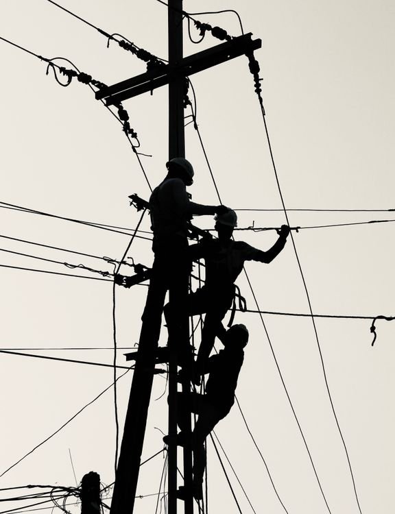 Silhouetted workers repairing electrical power lines on a utility pole